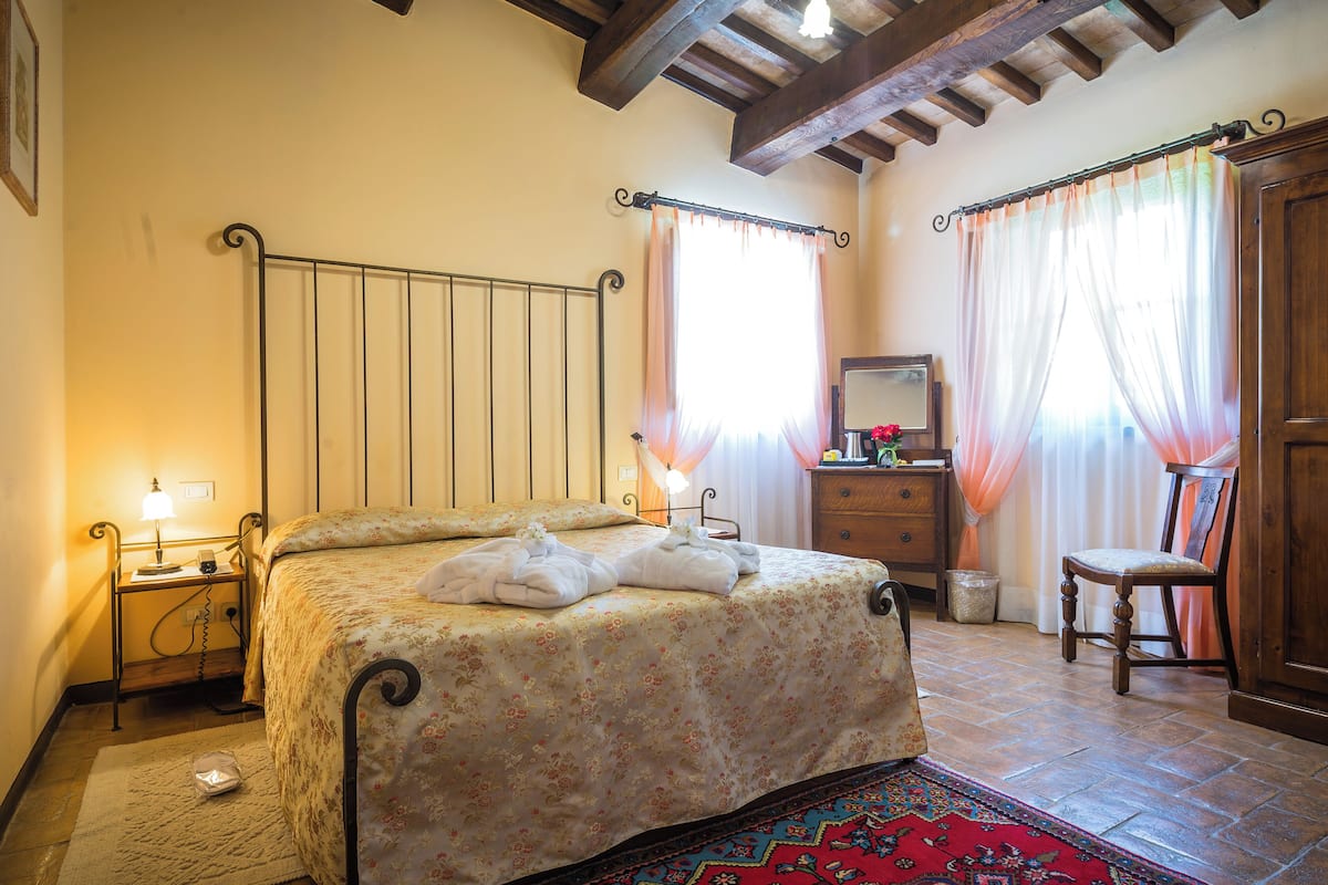 A bedroom with a bed, bedside table, lamp, chair, and a wooden cabinet.