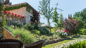 Un jardin agrémenté d’un bâtiment en briques, de murs en pierre et de diverses plantes et fleurs.