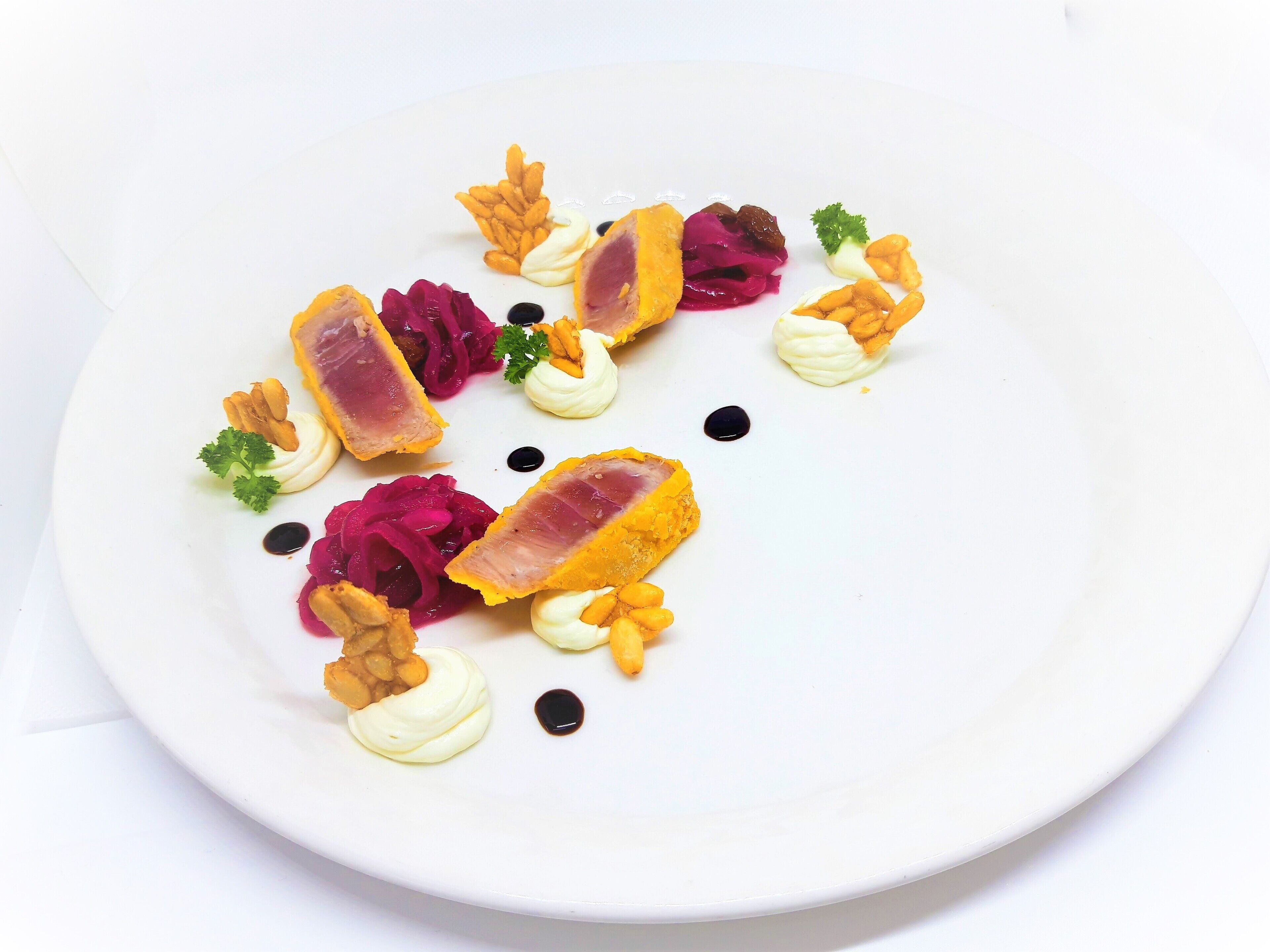 A white plate with various food items including slices of meat, cream, and vegetables.