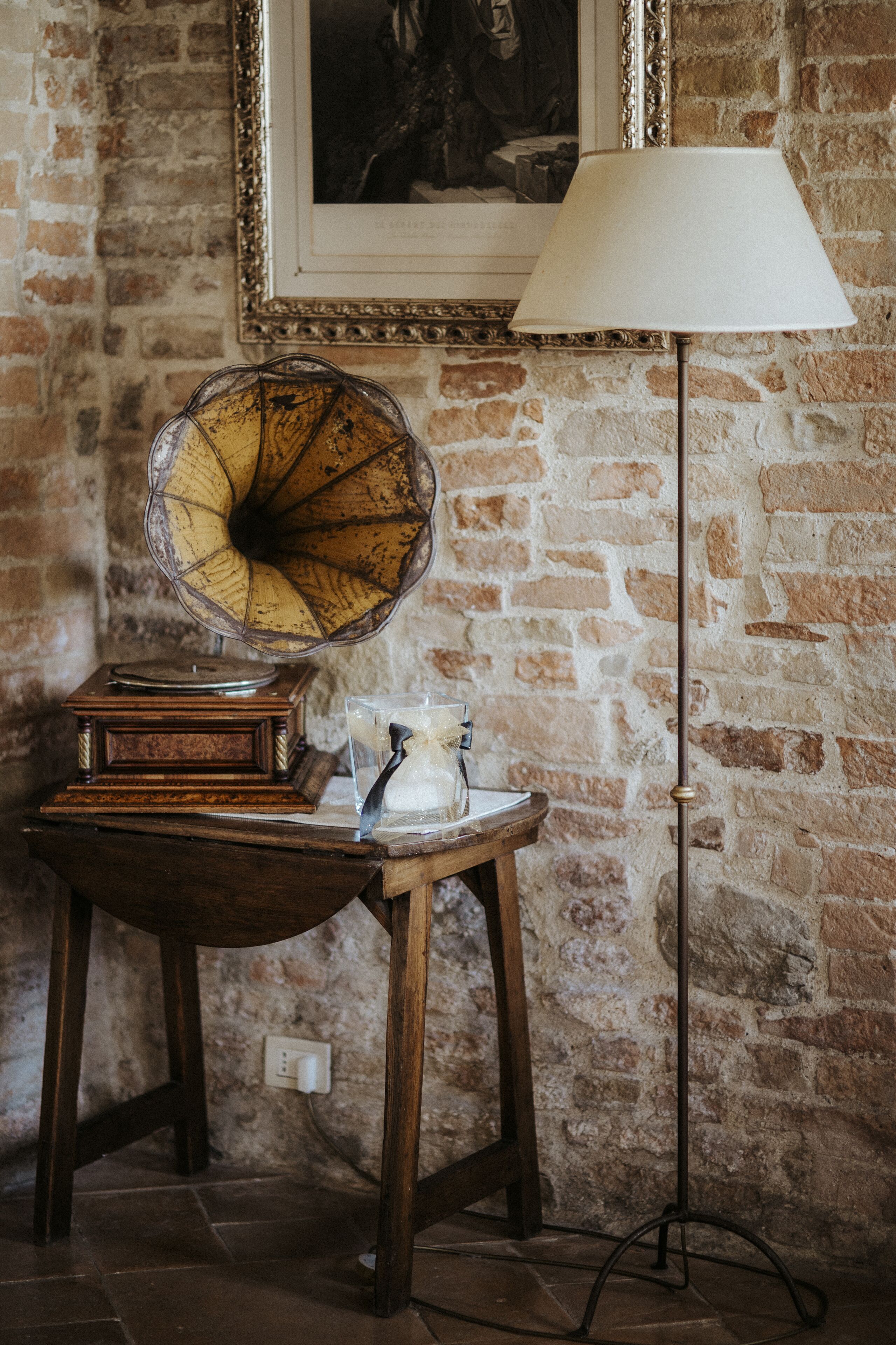 Un gramófono antiguo sobre una mesa de madera con una lámpara y un recipiente de vidrio.