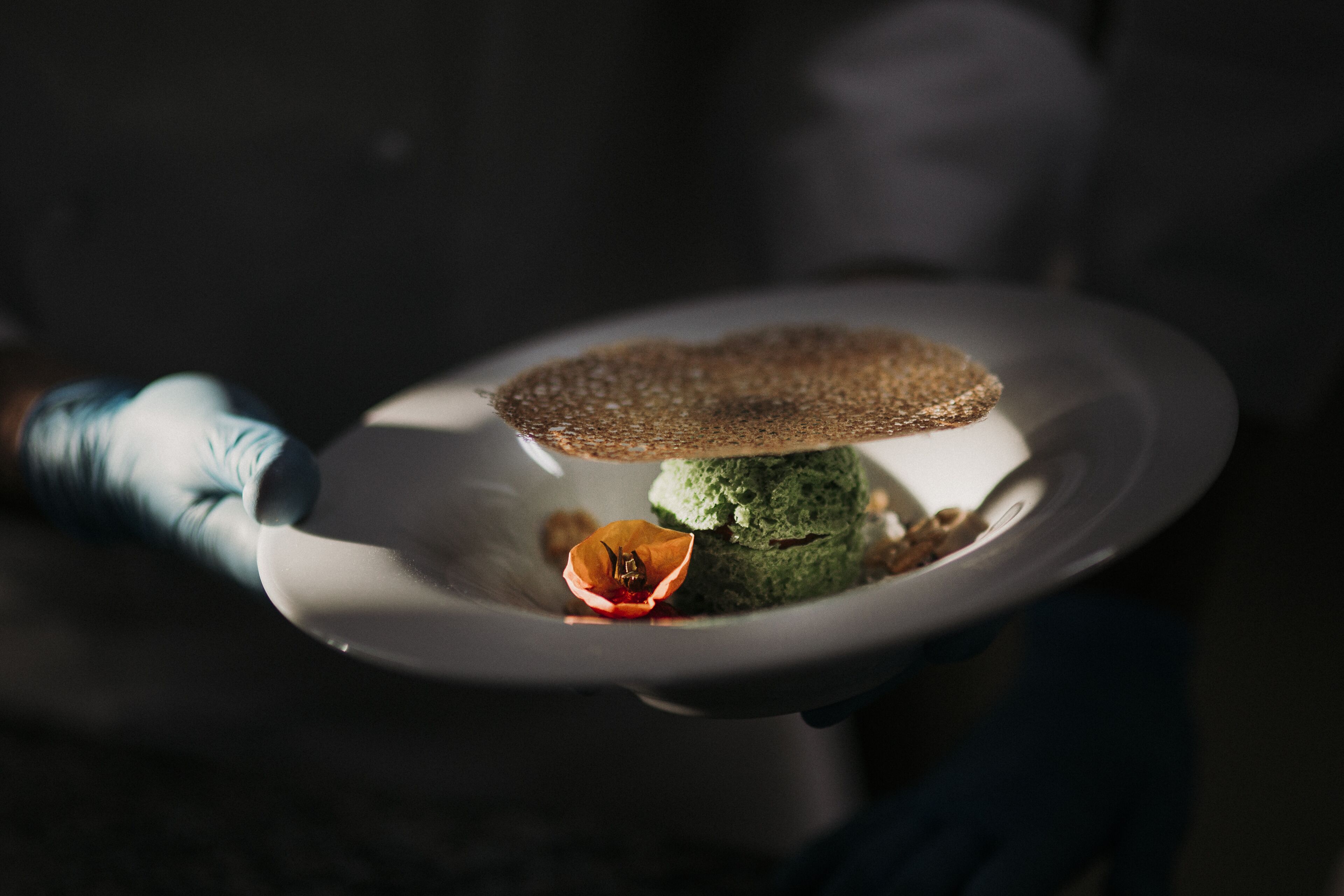 A plate with a green dessert and a brown topping, held by a person wearing a blue sleeve.