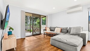 Un salon moderne avec un canapé gris, une table basse en bois et un téléviseur posé sur un meuble.