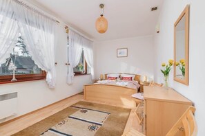 Un dormitorio con cama, mesita de noche, cómoda, ventana con cortinas y lámpara colgante.