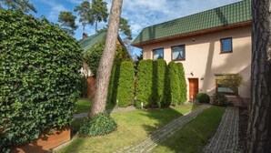 Een huis met een verharde oprit, een groen dak en een verzorgde tuin met hagen en bomen.