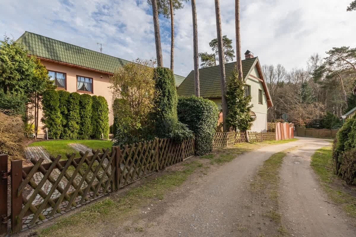 Een landweg die naar een huis met een groen dak leidt, omringd door hoge bomen en een houten hek.