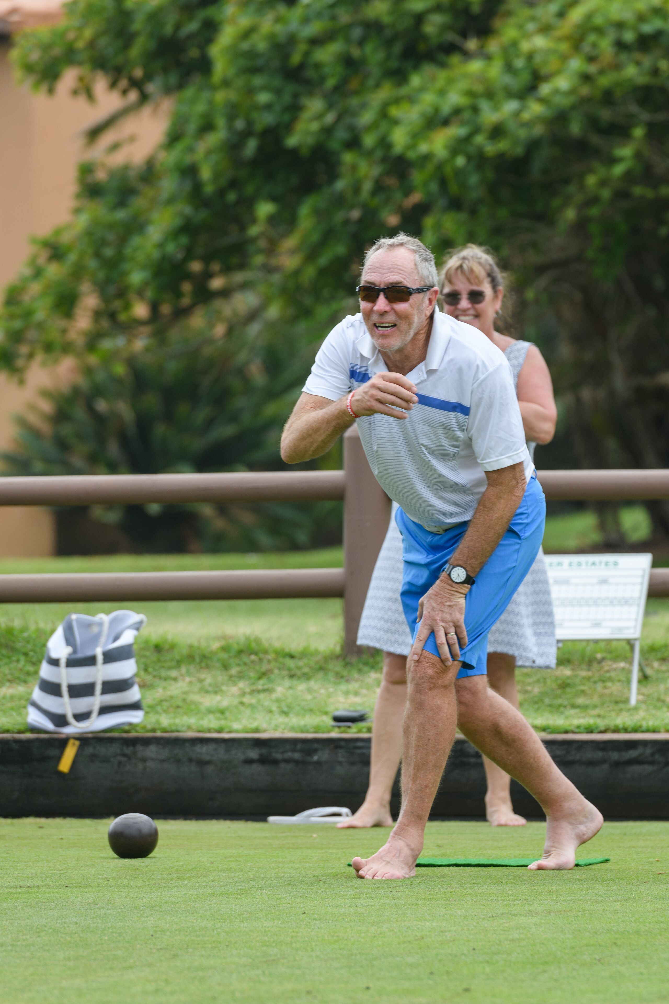 A man playing croquet barefoot on a grassy field with a ball and a mallet.