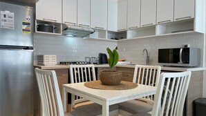 A modern kitchen with white cabinetry, a stainless steel refrigerator, a microwave, and a dining table with chairs. - Marassi Marina 2 bedroom pool view 403 (El Alamein)