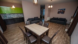 A modern kitchen with green cabinets, a dining area with a wooden table and chairs, and a living area with a sofa and a painting on the wall.