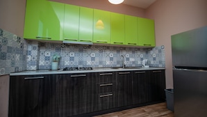 A kitchen with green cabinets, a tiled backsplash, a stainless steel refrigerator, and a wooden floor.