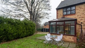 Ein Backsteinhaus mit Wintergarten und einer Terrasse mit weißen Stühlen.