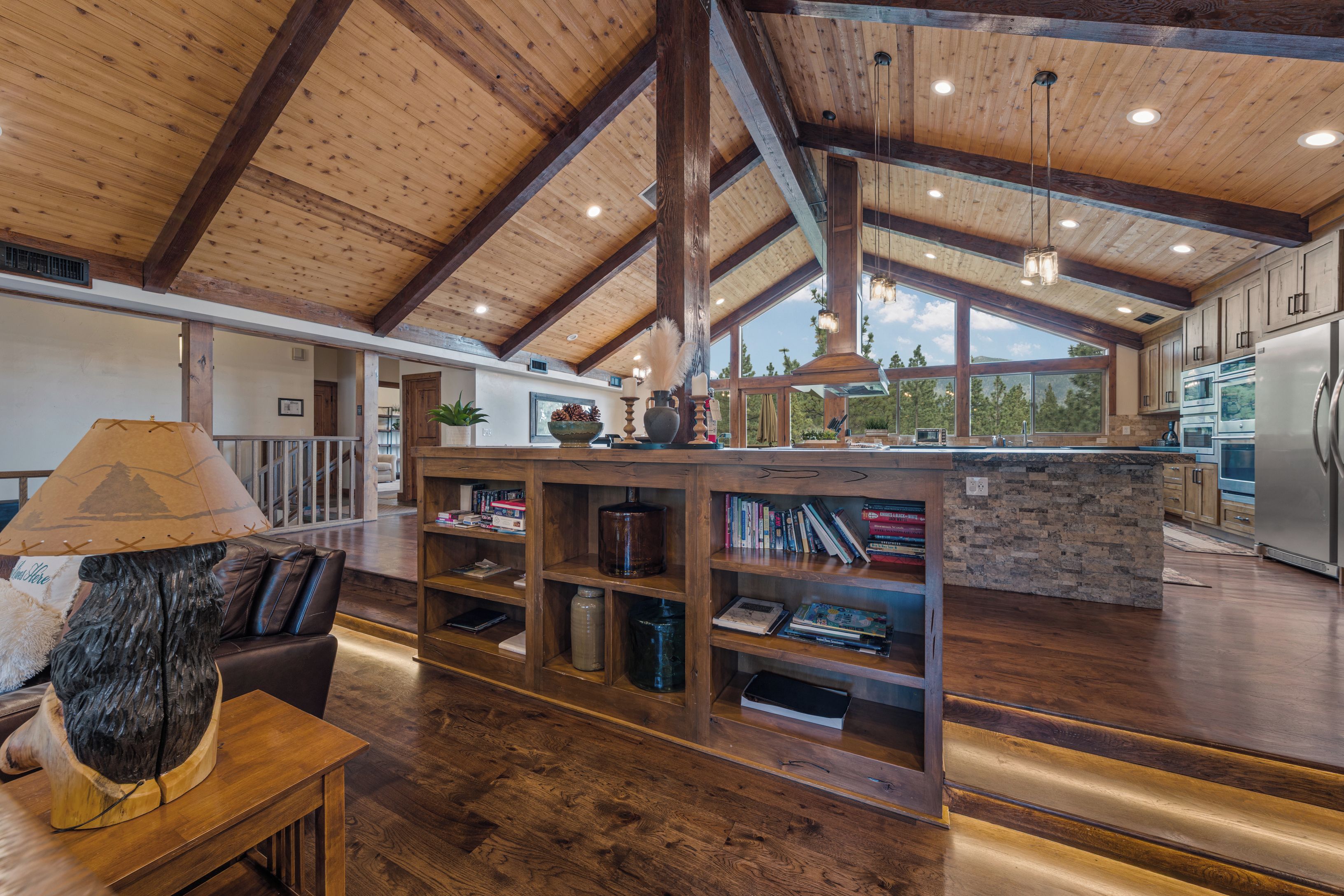 A spacious living area with a high ceiling, wooden beams, and a central island with bookshelves.