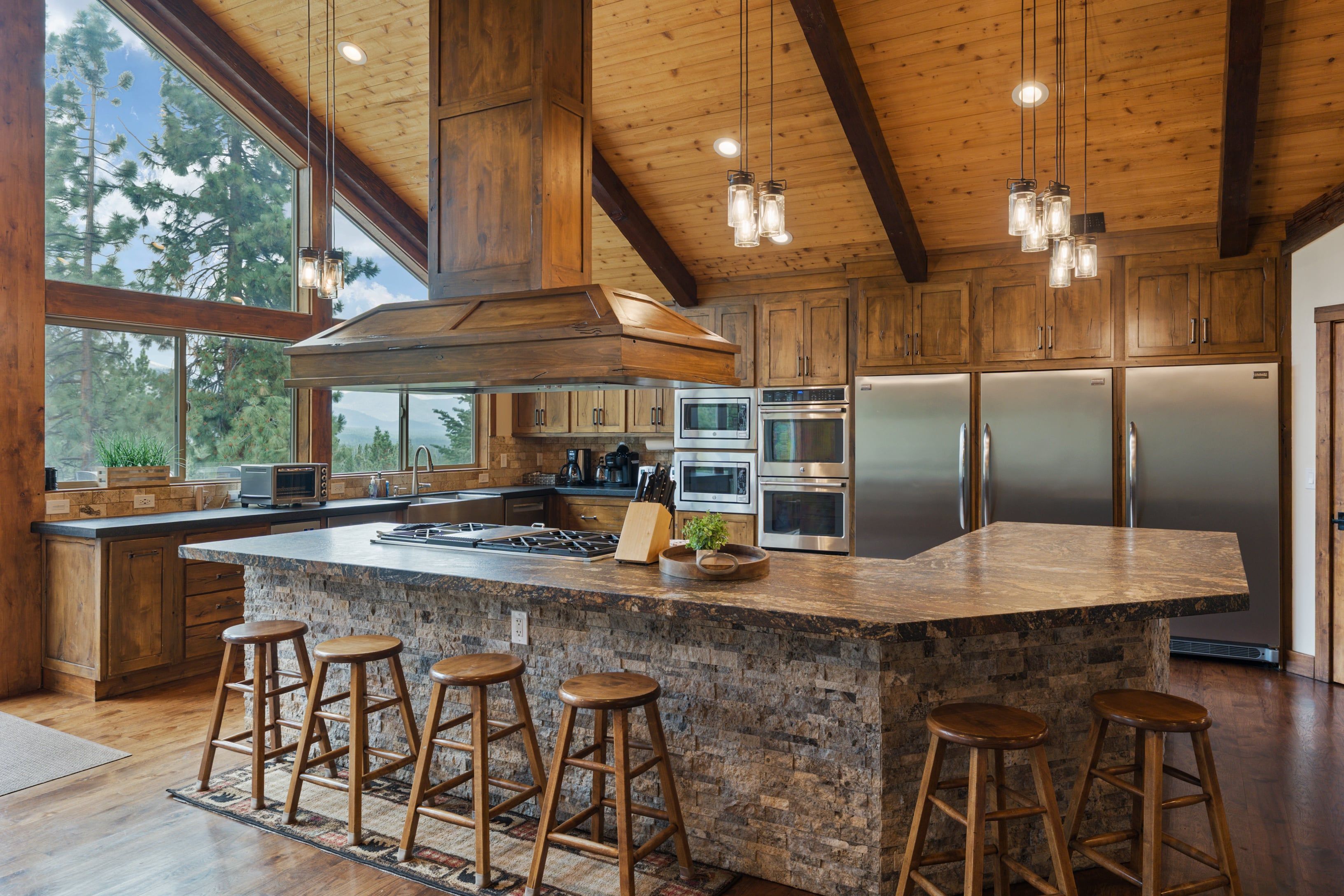 A spacious kitchen with a large island, wooden cabinets, stainless steel appliances, and a view of the outdoors through large windows.