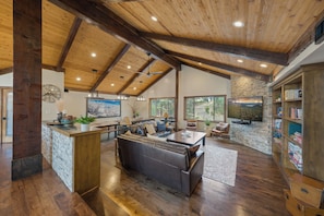 A spacious living area with a high ceiling, wooden beams, a large leather sofa, a dining table, and a bookshelf.