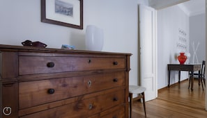 Uma cômoda de madeira com várias gavetas, um vaso branco e um quadro pendurado na parede.