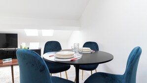 Ein moderner Essbereich mit einem runden Tisch, blauen Samtstühlen und einem Flachbildfernseher im Hintergrund.
