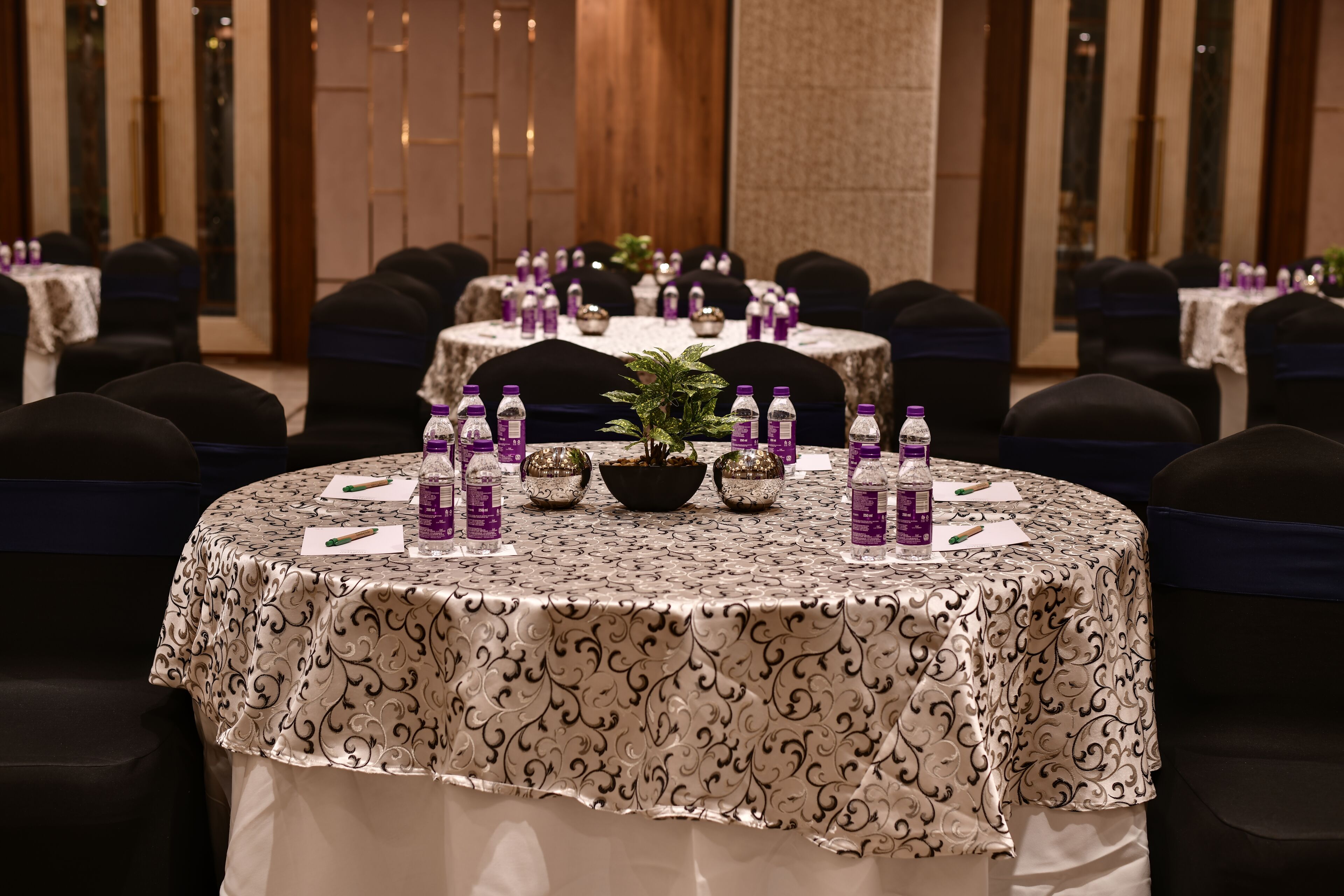 Un salón de conferencias con mesas redondas, cada una con botellas de agua, bolígrafos y blocs de notas.