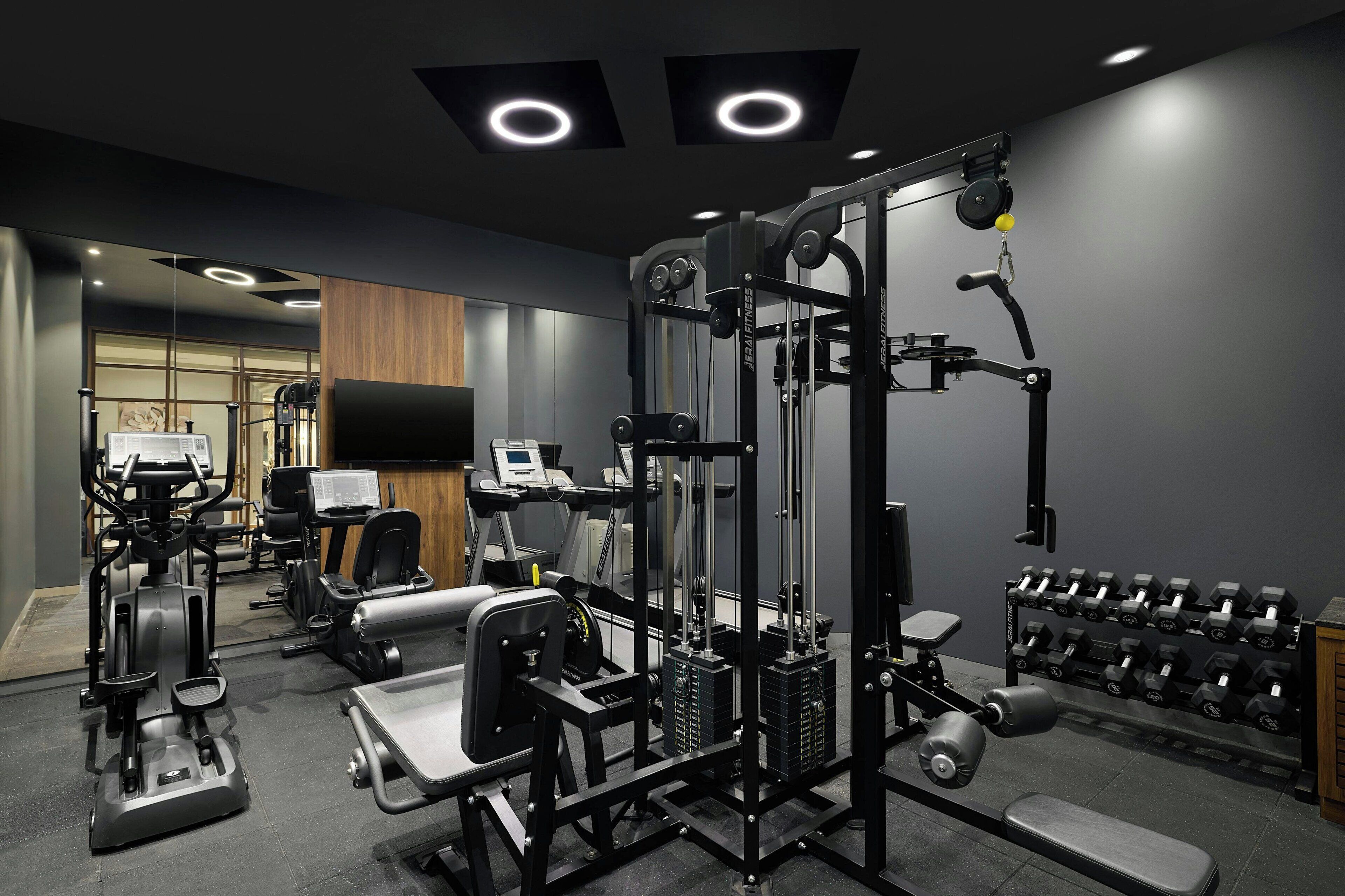 A gym with various exercise equipment, including a cable machine, treadmills, and dumbbells.
