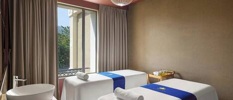 Habitación de hotel con dos camas, un ventanal con cortinas, un lavamanos y una mesita con artículos de aseo.