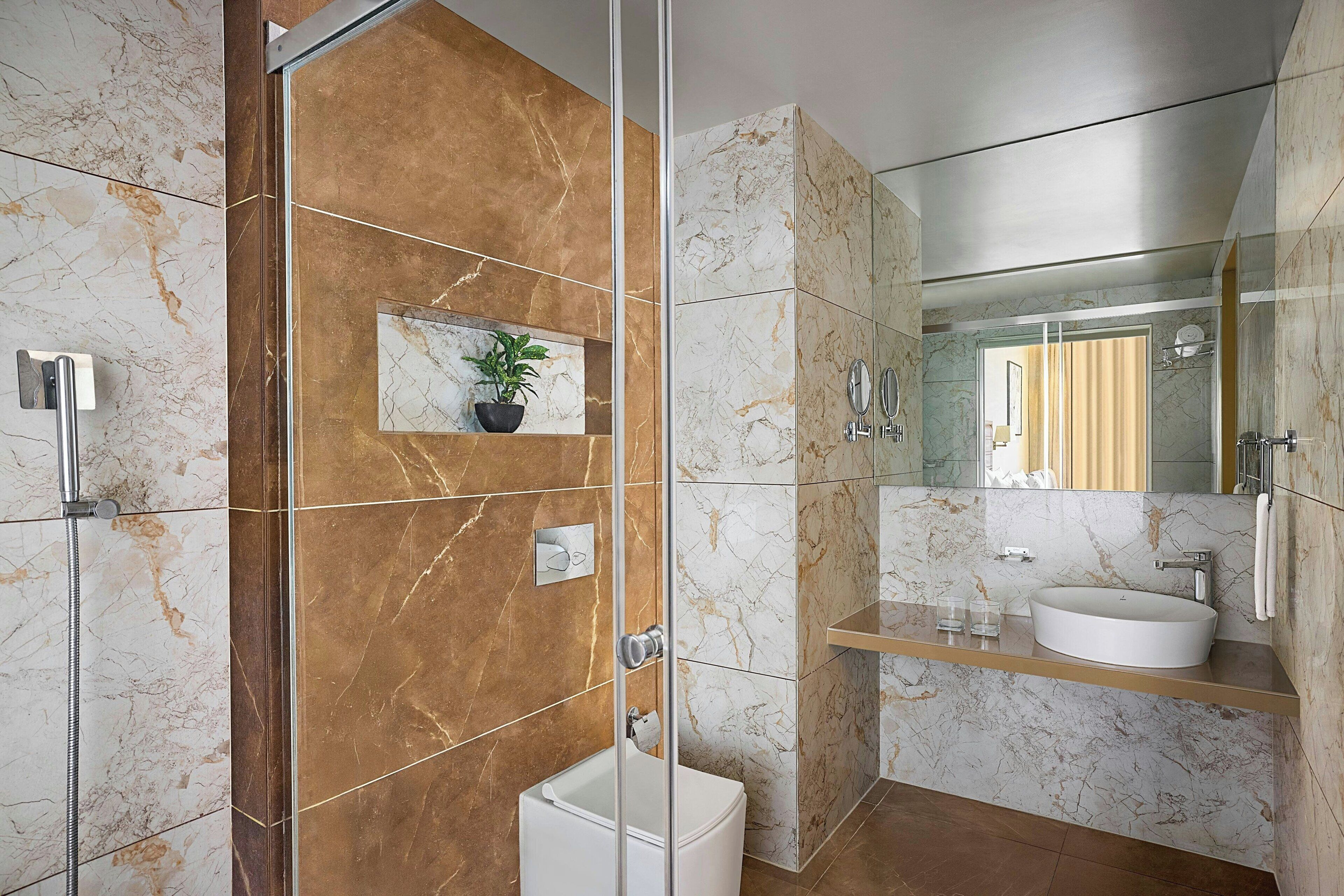 A modern bathroom with a glass-enclosed shower, a white sink, and a marble-tiled wall.