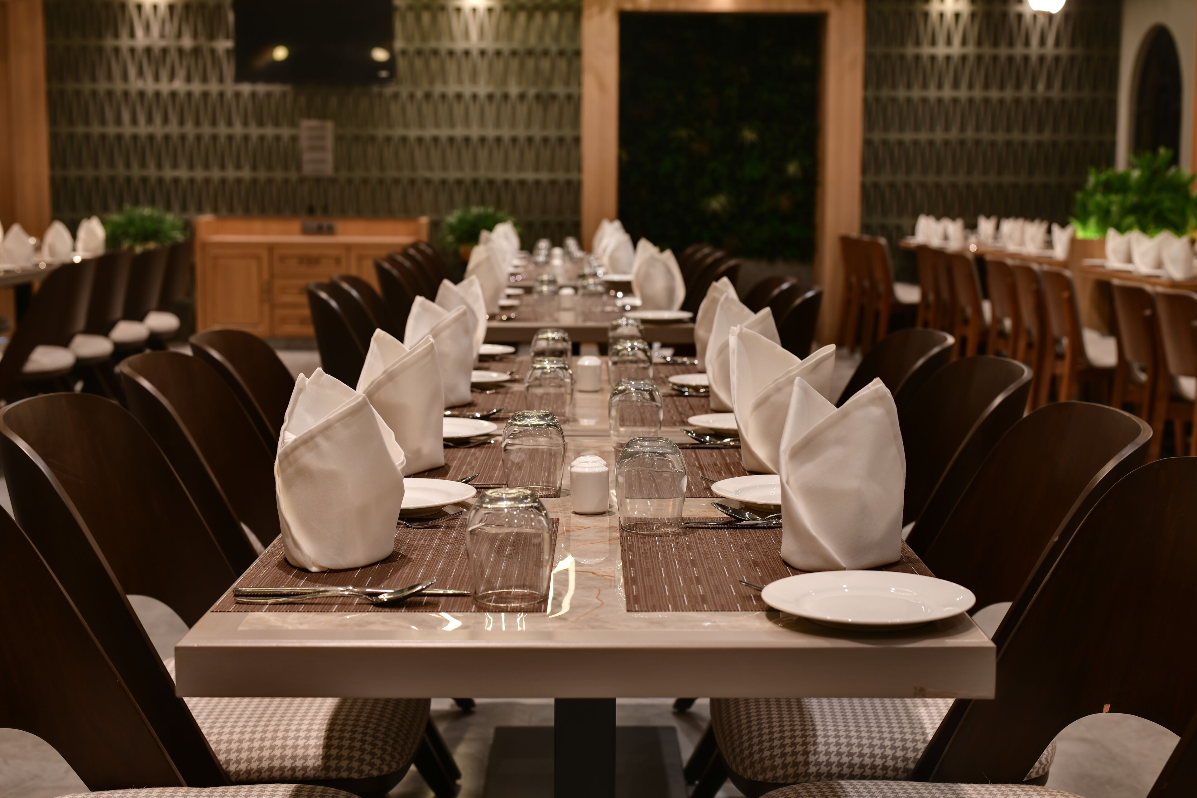 A long dining table set with white napkins, plates, and cutlery, surrounded by chairs with cushioned seats.