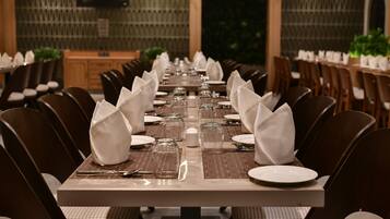 A long dining table set with white napkins, plates, and cutlery, surrounded by chairs with cushioned seats.
