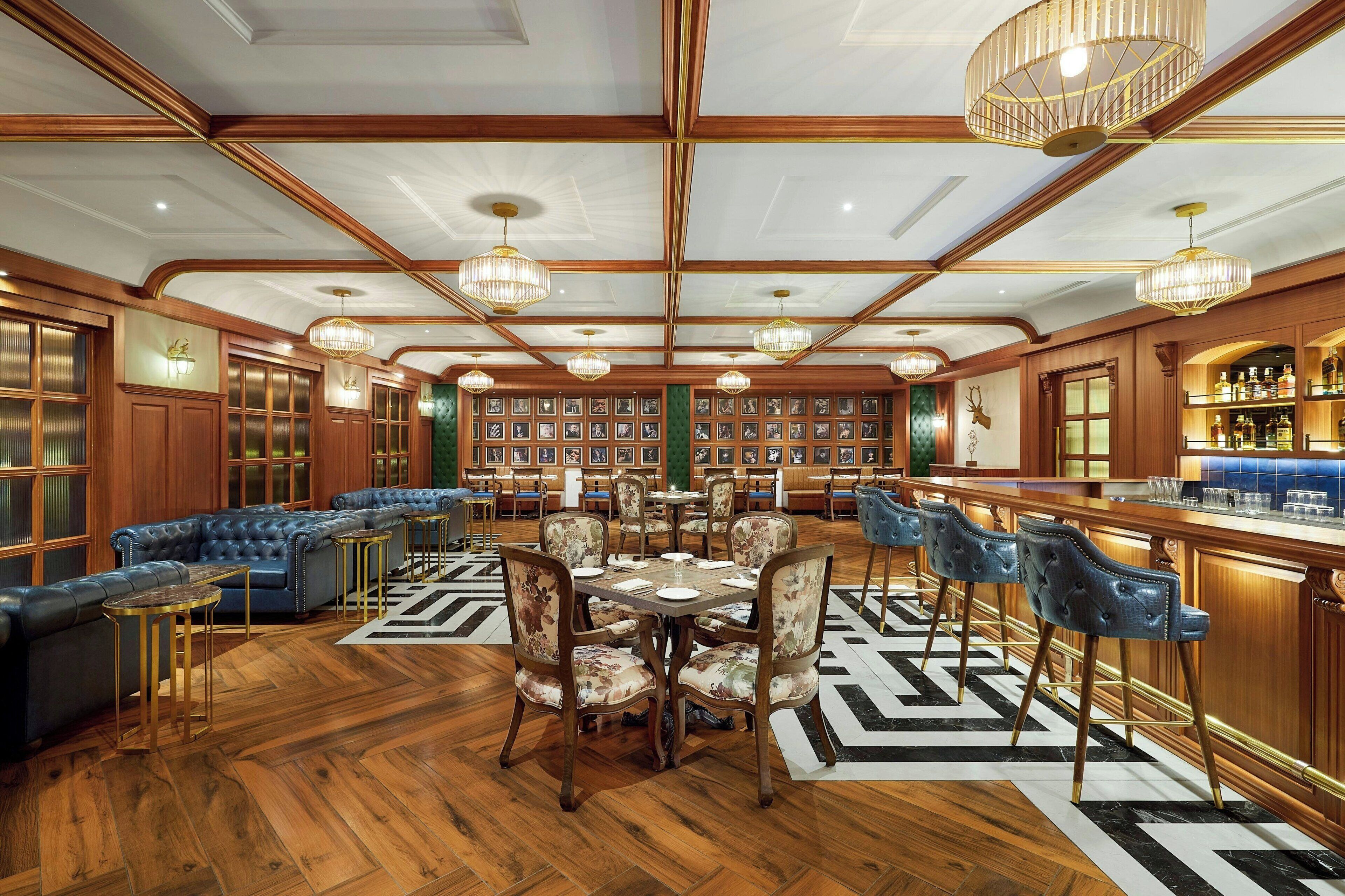 A spacious room with a wooden ceiling, a bar area with a liquor display, a seating area with a blue sofa and floral chairs, and a wall of framed pictures.