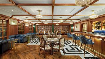 A spacious room with a wooden ceiling, a bar area with a liquor display, a seating area with a blue sofa and floral chairs, and a wall of framed pictures.