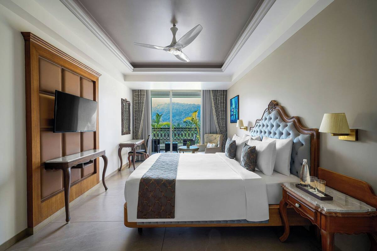 Ein Hotelzimmer mit einem großen Bett, einem Deckenventilator, einem Fernseher, einem Balkon mit Aussicht und einem Schreibtisch mit Lampe.