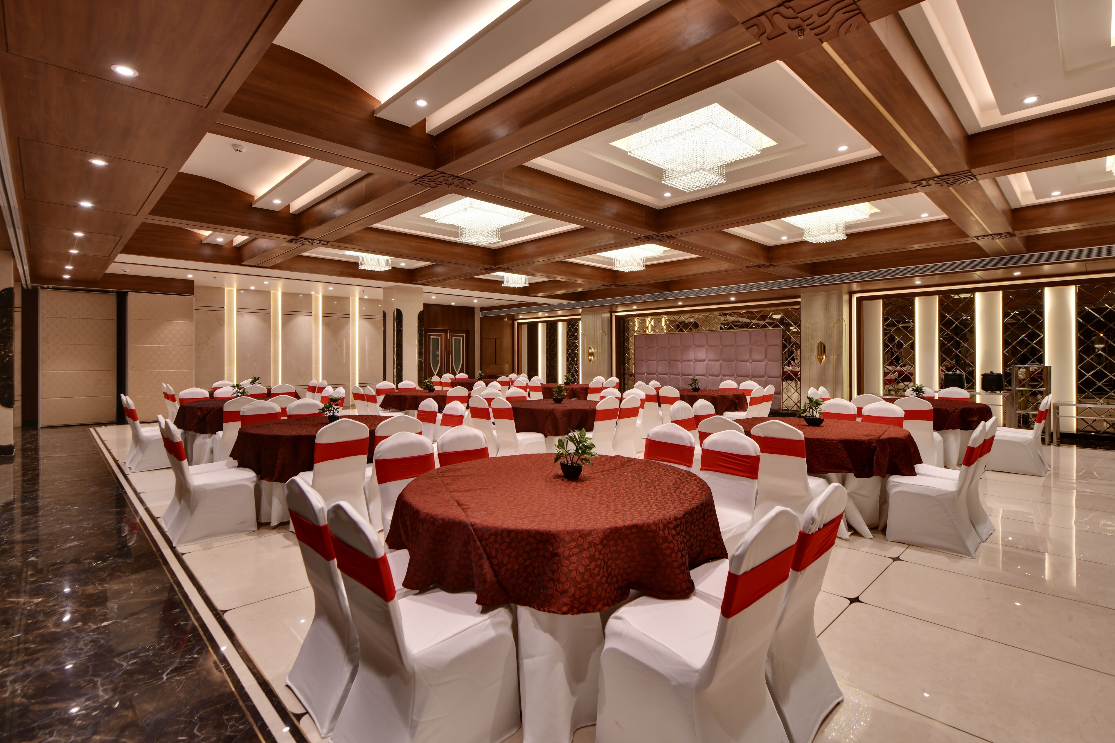 A banquet hall with round tables, white chairs, and red sashes.