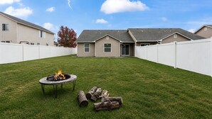 Ein Garten mit Feuerstelle, Holzscheiten und einem weißen Zaun.