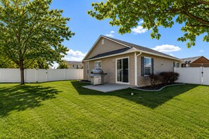 A single-story house with a covered patio, a barbecue grill, and a white fence.