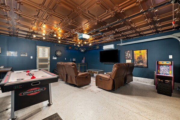 A room with a pool table, comfortable seating, a projector, and a TV.