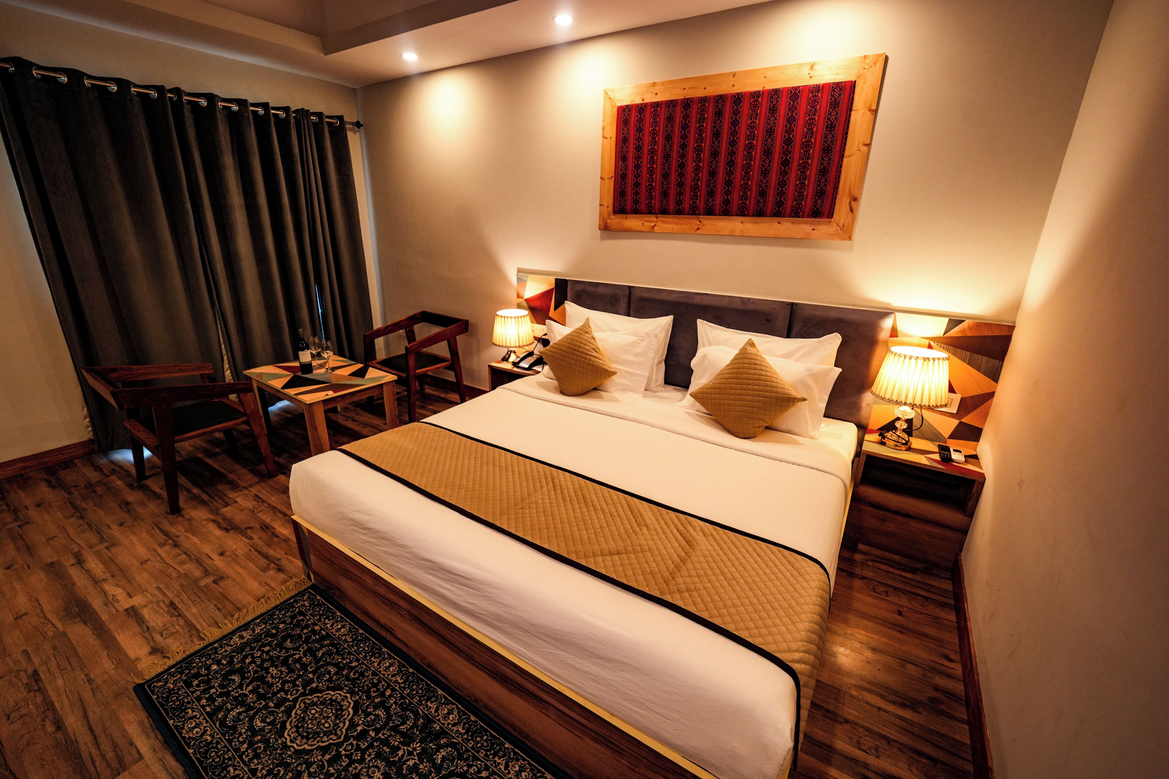 A hotel room with a large bed, a desk, a chair, and a nightstand with lamps.
