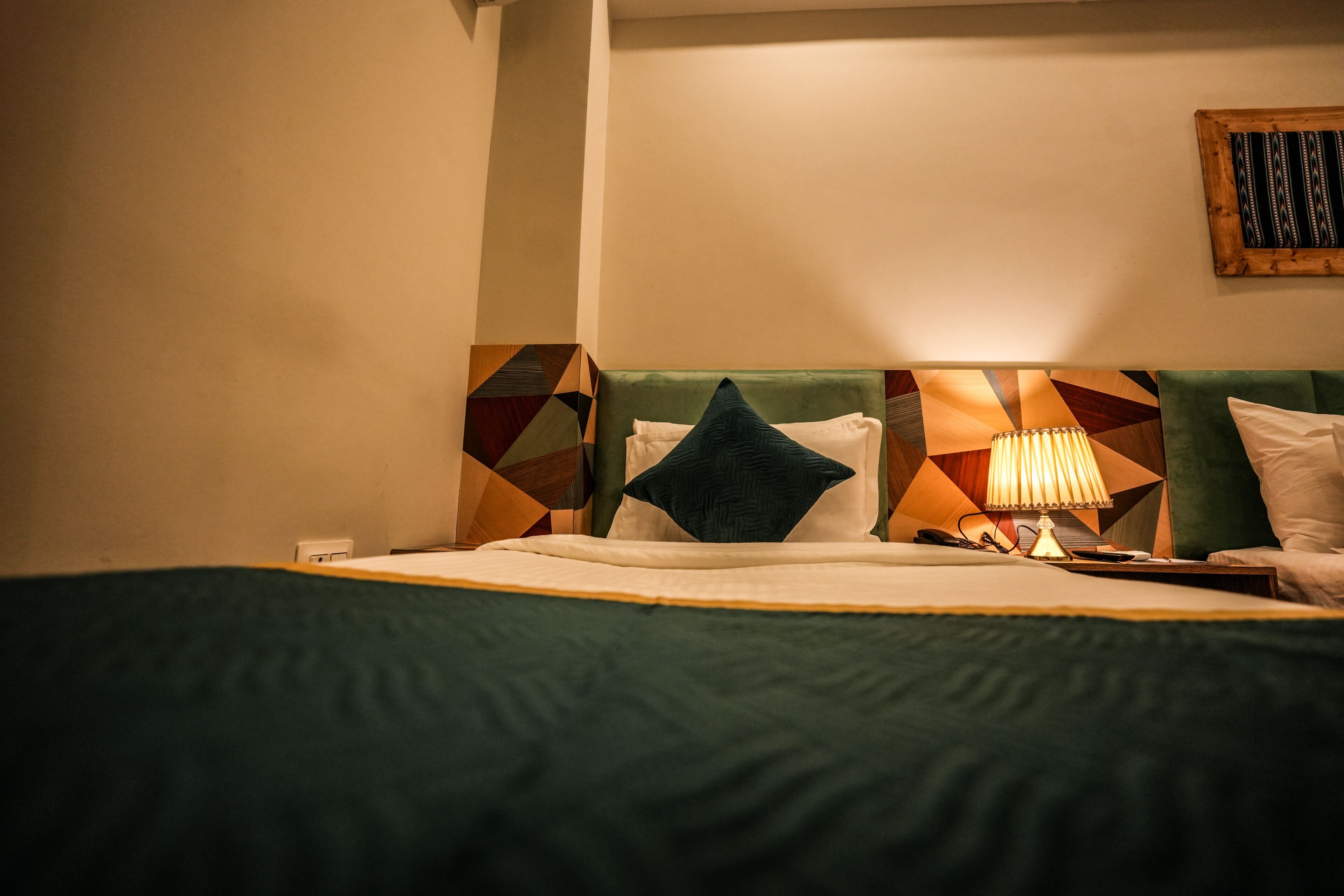 Une chambre d’hôtel comprenant un lit, une table de chevet, une lampe et une tête de lit ornée d’un motif géométrique.