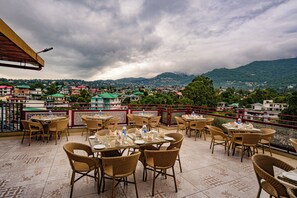 A terrace with tables and chairs, overlooking a town and mountains. - Hotel Square One By D'Polo Dharamshala  ID 92552899 (Dharamshala)
