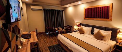 A hotel room with a bed, a desk, a TV, a ceiling fan, and a wall-mounted artwork.