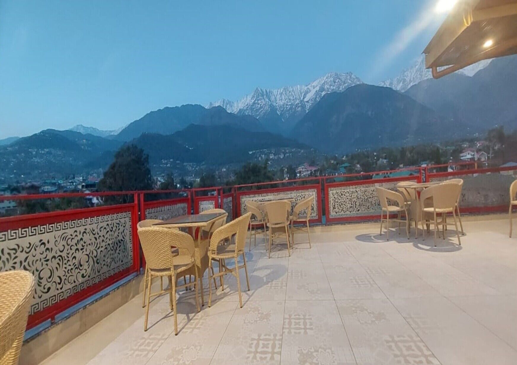 A terrace with wicker chairs and tables, overlooking a mountainous landscape with snow-capped peaks.