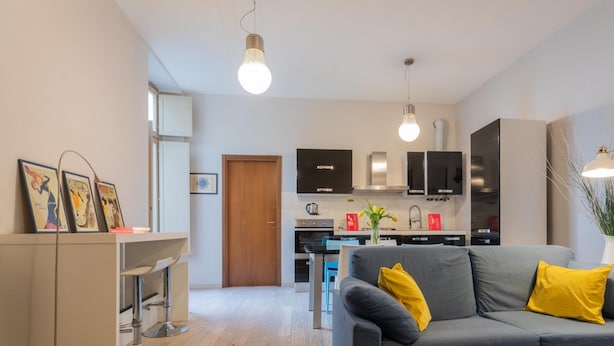 A modern living room with a grey sofa, yellow cushions, and a dining area with a table and chairs. - La Maison du Vent by Wonderful Italy (Turin)