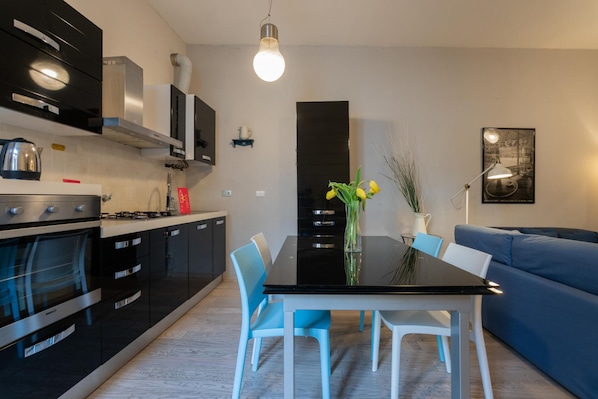 A modern kitchen with black cabinets, a stainless steel oven, and a black dining table with white chairs.