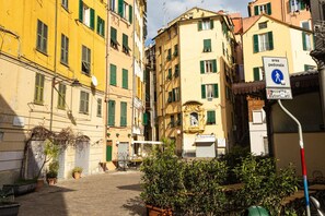 A narrow street with buildings on either side, a pedestrian crossing sign, and outdoor seating with tables and chairs.