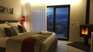 A hotel room with a large bed, a fireplace, a view of a snowy landscape, and a red accent wall. - Villa Regadio (Covilhã)