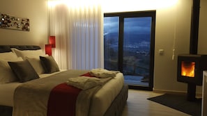 Relax in a spacious room with a large bed, wood-burning stove, and sliding glass door leading to a balcony with a view.