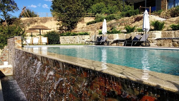 A swimming pool with a waterfall feature, lounge chairs, and umbrellas. - Villa Regadio (Covilhã)
