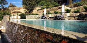 A swimming pool with a waterfall feature, lounge chairs, and umbrellas.