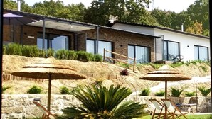 A modern house with a stone facade, large windows, and a well-maintained garden with umbrellas and seating. - Villa Regadio (Covilhã)