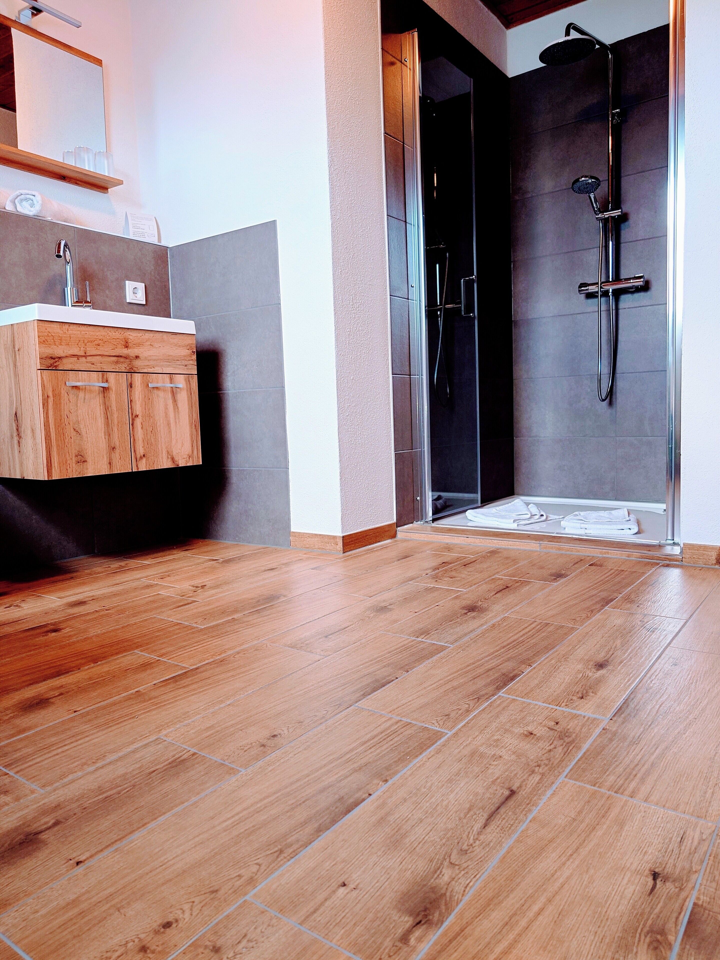 Un baño con tocador de madera, ducha con cabezal de ducha de mano y suelo de baldosas.