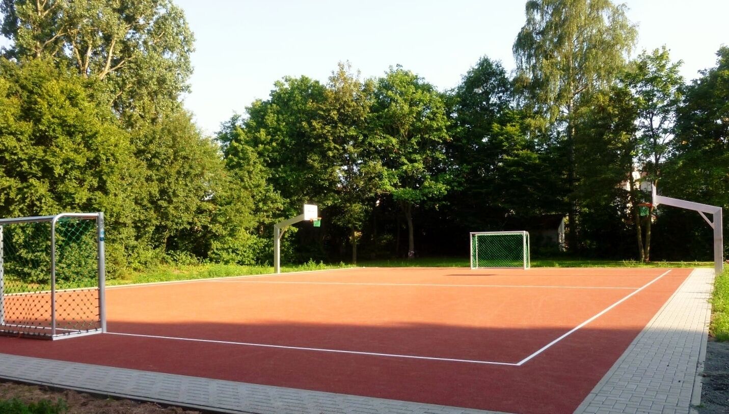 An outdoor tennis court with two goals, surrounded by trees.