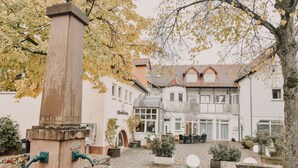 A courtyard with a fountain, potted plants, and a building with multiple windows and a balcony. - Hotel Schlemmerscheune (Weilerbach)