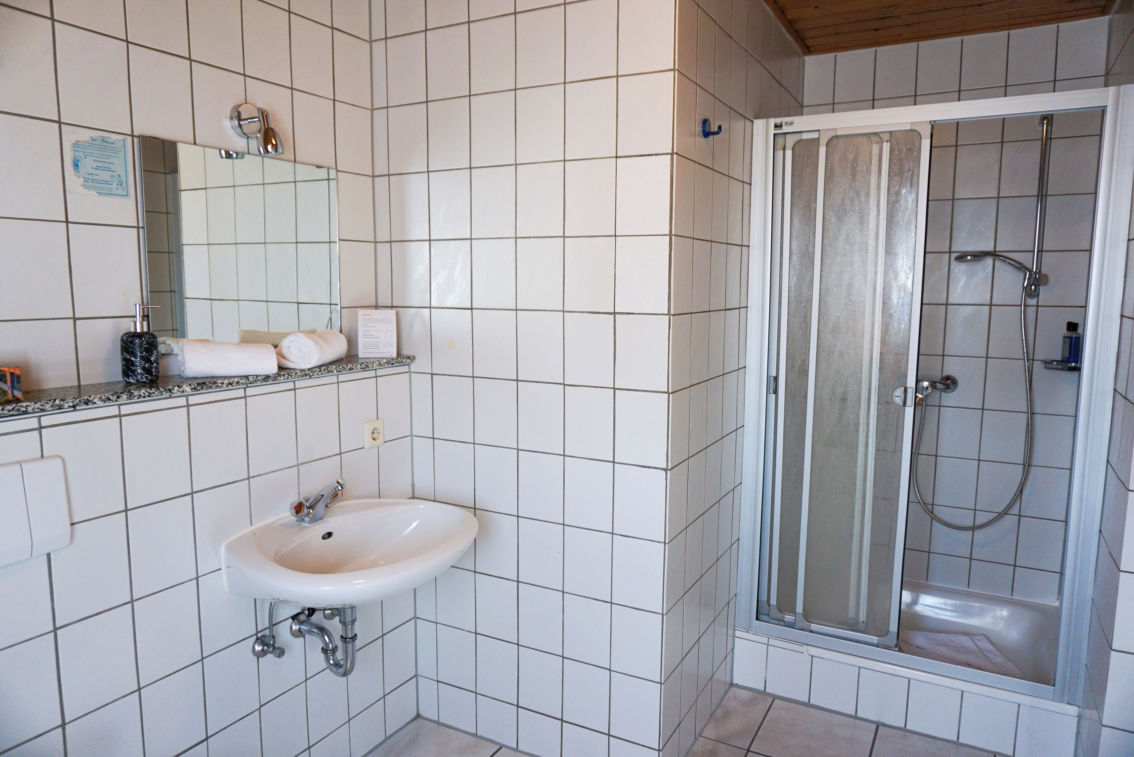 A bathroom with white tiles, a sink, a mirror, and a glass-enclosed shower.