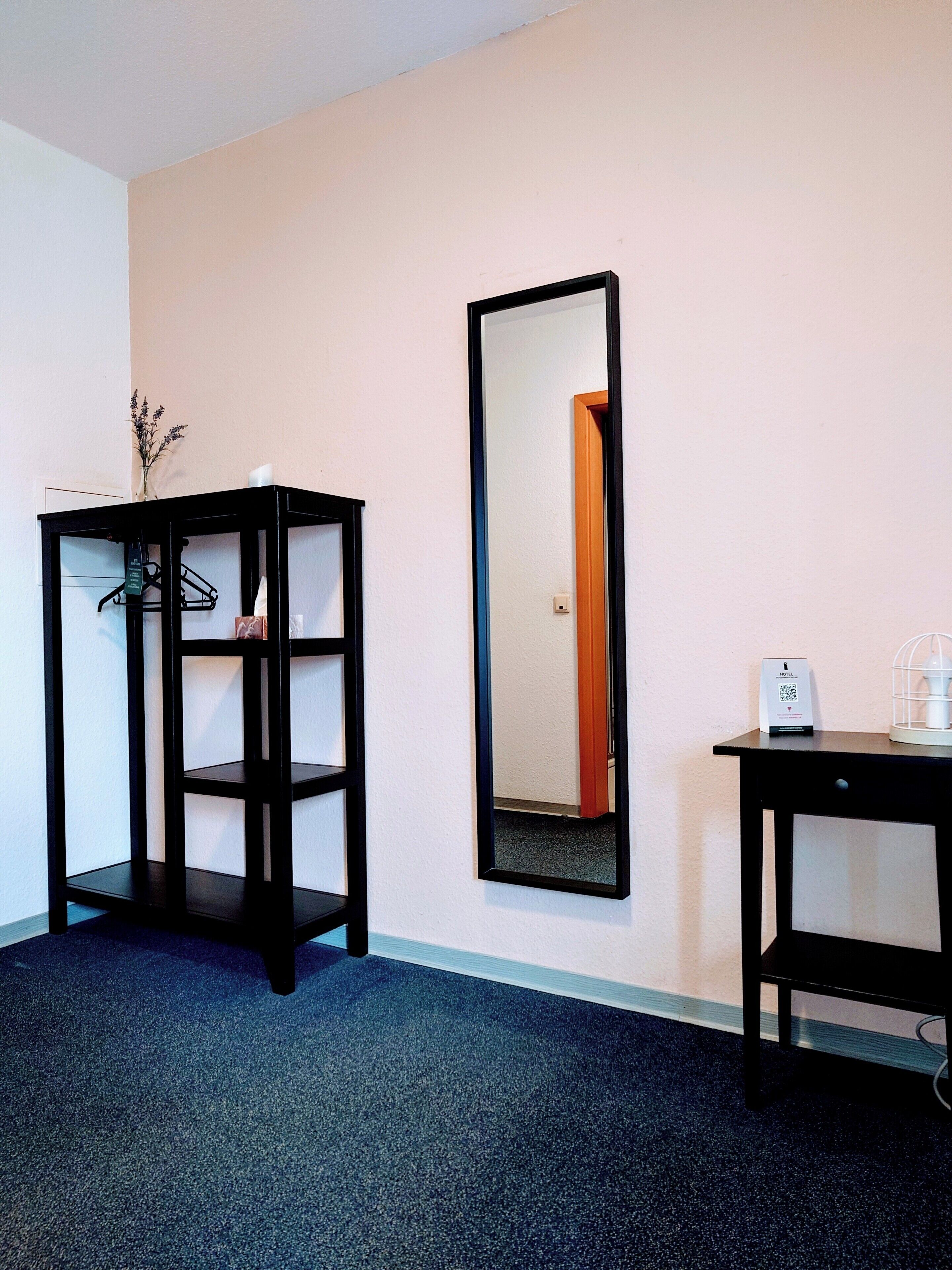Ein Zimmer mit einem schwarzen Regalelement, einem Spiegel und einem kleinen Tisch mit einem weißen Gegenstand darauf.